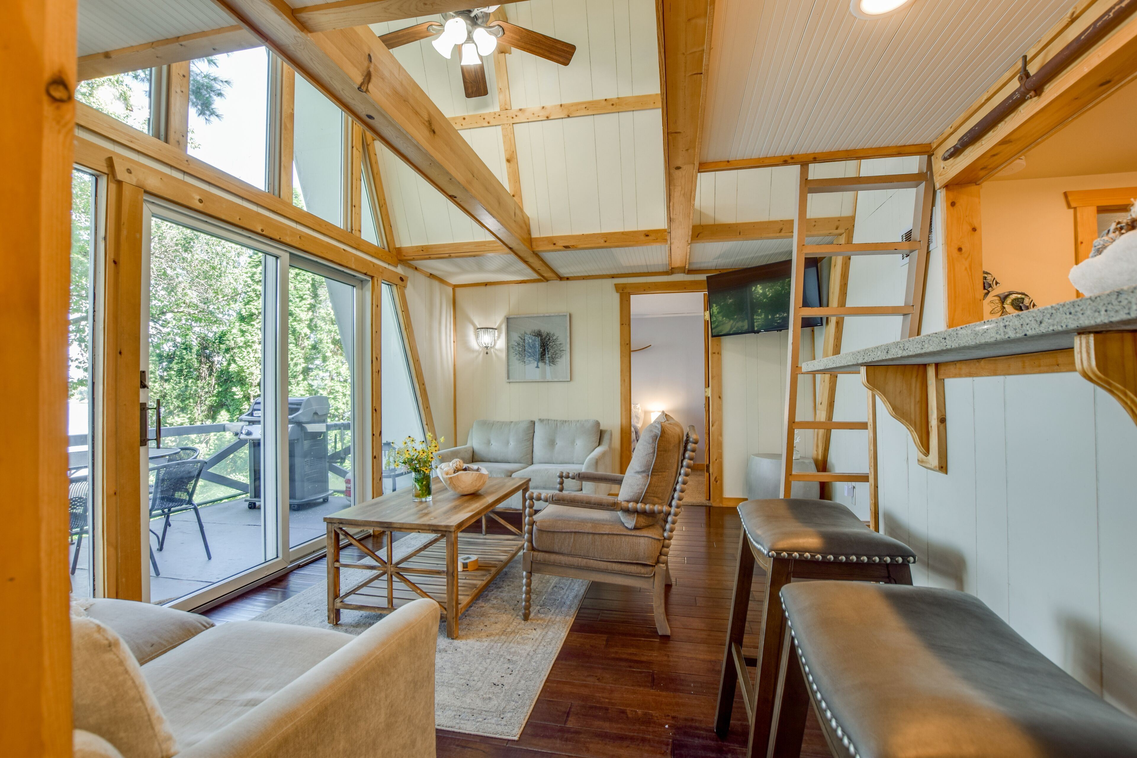 Un intérieur chaleureux avec un plafond en bois, un coin repas et un espace salon comprenant un canapé et des fauteuils.