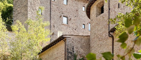 Um edifício de pedra com várias janelas e uma torre, rodeado por vegetação.