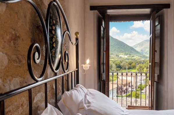 A room with a bed, a view of a mountainous landscape through an open door, and a balcony with a railing. - Antica Torre Del Nera (Scheggino)