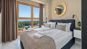 Een hotelkamer met een groot bed, een ronde spiegel en uitzicht op de stad door een groot raam.