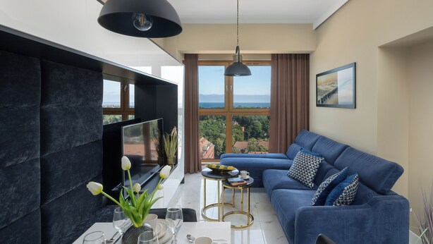 Een moderne woonkamer met een blauwe bank, een flatscreen televisie en een eethoek met een tafel en stoelen.