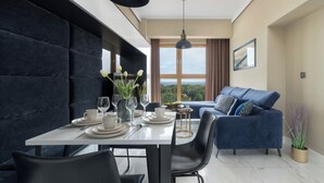 Een moderne eethoek met een tafel gedekt voor twee personen, een blauwe bank en een groot raam met uitzicht op het landschap.