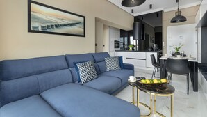 Een moderne woonkamer met een blauwe bank, een eethoek met een tafel en stoelen, en een keuken op de achtergrond.