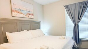 Un dormitorio limpio y bien iluminado, con una cama bien hecha, un cuadro en la pared y una ventana con cortinas.