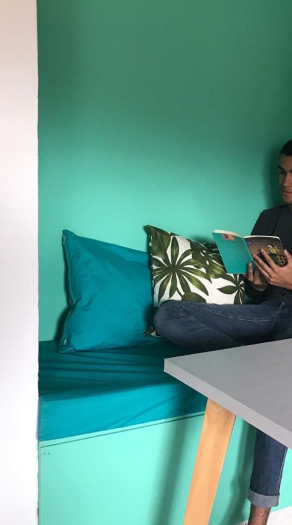 Una persona sentada en un sofá azul verdoso con un cojín de estampado verde y blanco, leyendo un libro.