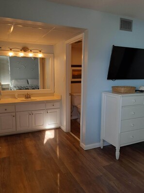 A bathroom with a vanity, mirror, and a toilet visible through an open door.