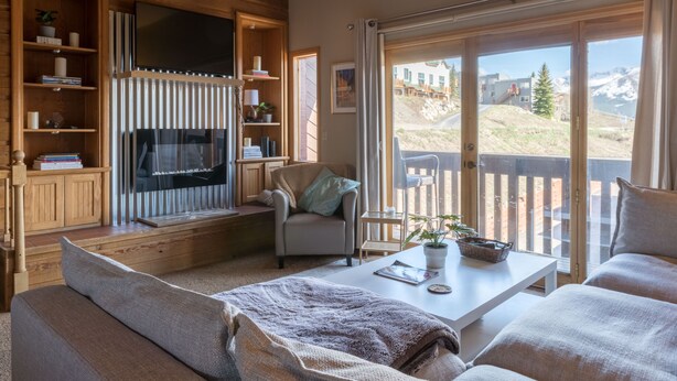 Een gezellige woonkamer met een open haard, comfortabele zithoeken, een televisie en een groot raam met uitzicht op de bergen.
