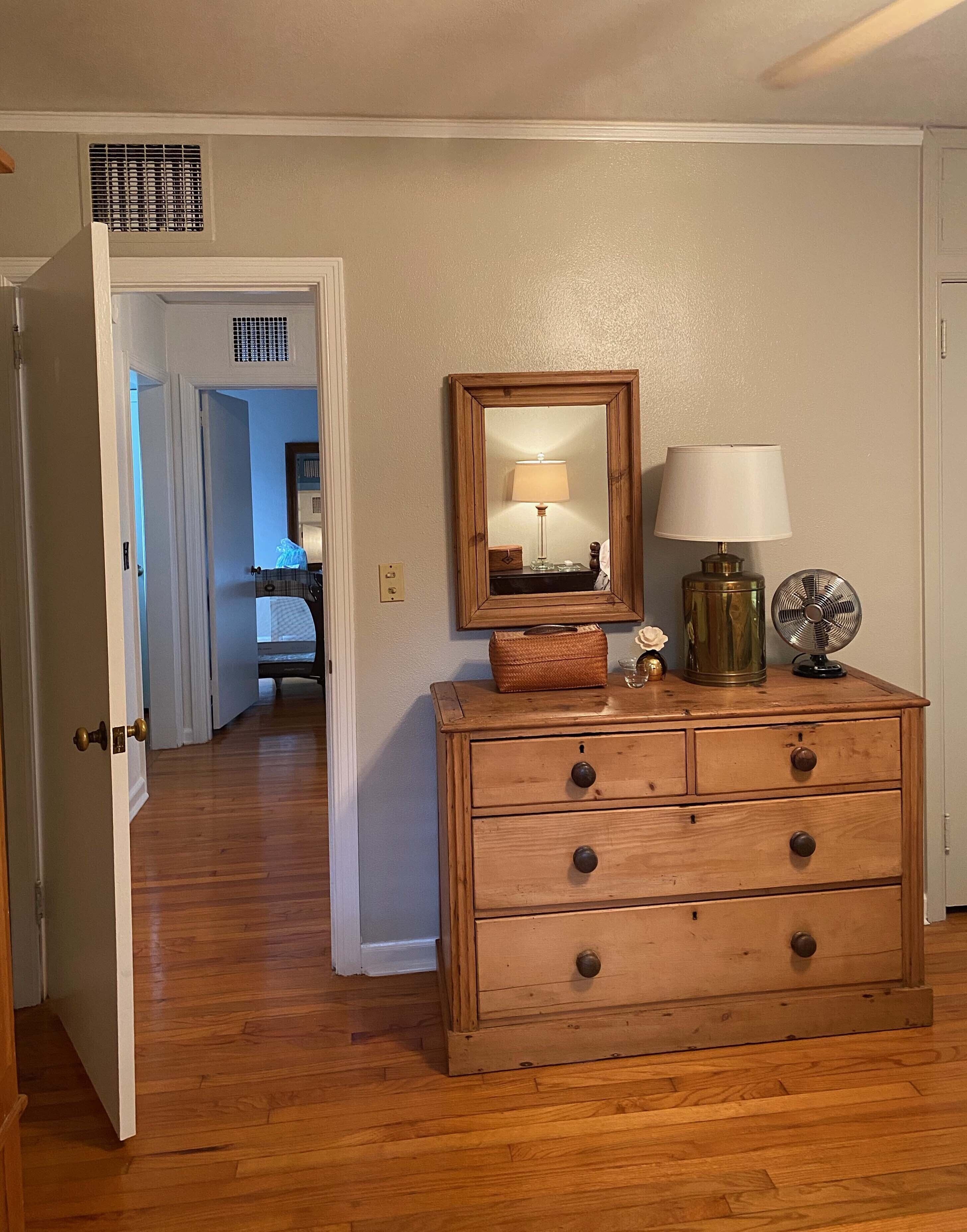 A wooden dresser with drawers, a mirror, a lamp, and a fan.