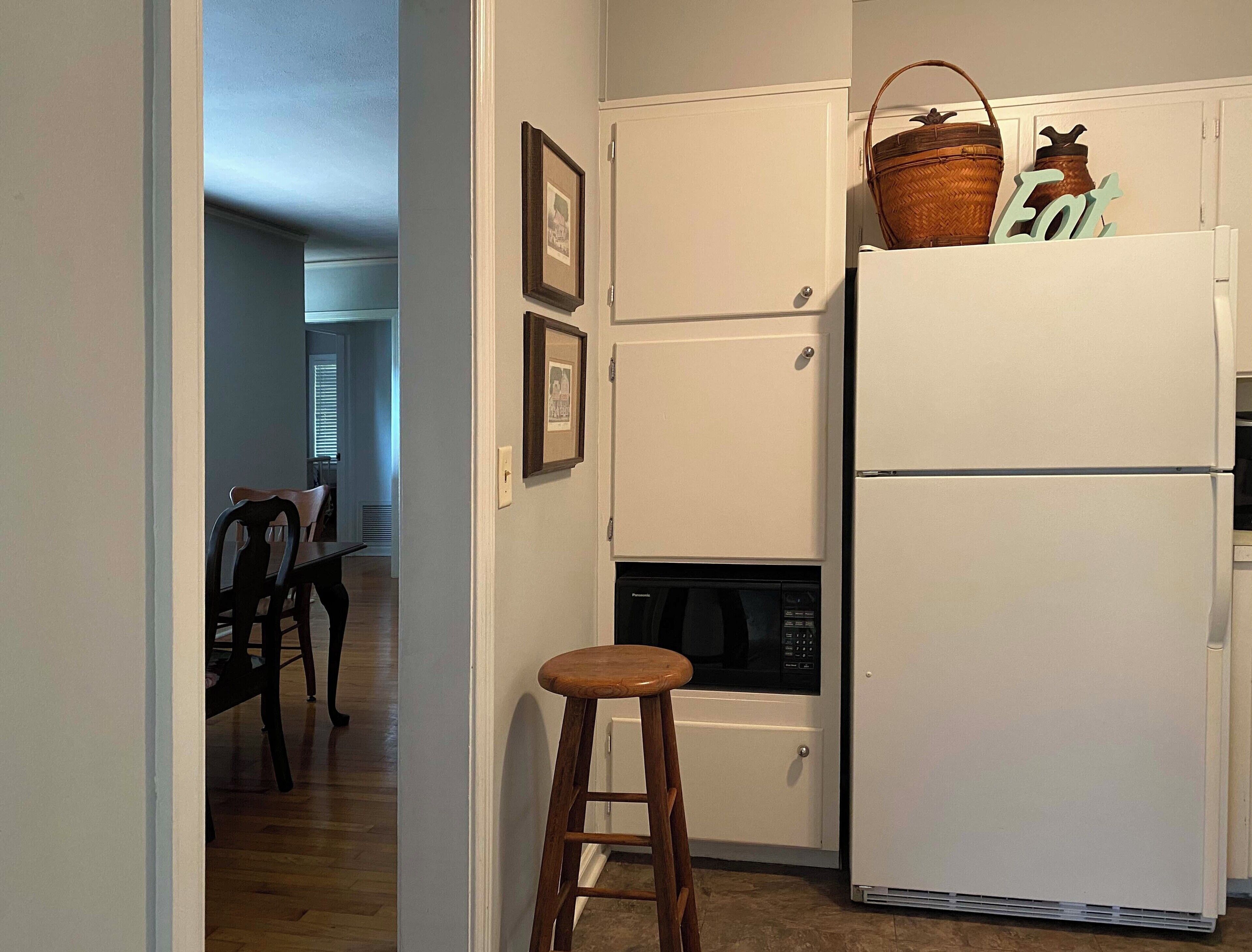 Una cocina compacta con un refrigerador blanco, un microondas y un pequeño comedor con una silla y una mesa de madera.