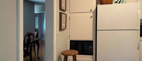 Una cocina compacta con un refrigerador blanco, un microondas y un pequeño comedor con una silla y una mesa de madera.