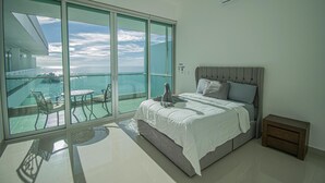 Ein Schlafzimmer mit einer großen Schiebeglastür, die auf einen Balkon mit Meerblick führt.
