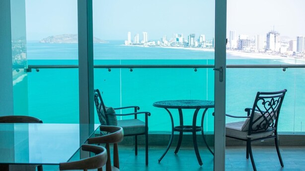 Un balcón con vista al océano y al horizonte de la ciudad, con una mesa y dos sillas.