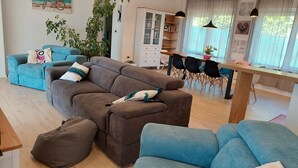 Un salon moderne avec un canapé marron, des fauteuils bleus, une table à manger en bois et un meuble blanc.