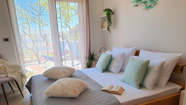 Une chambre à coucher avec un lit, des oreillers, une table de chevet, une chaise et une fenêtre donnant sur des arbres.