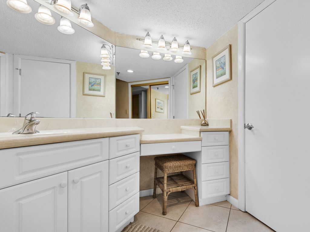 A bathroom with a double sink, white cabinets, a wicker stool, and framed artwork on the walls.