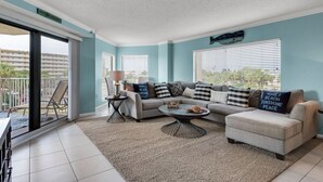 A modern living room with a sectional sofa, a coffee table, and a view of the outside balcony. - Gulf View, Updated Condo, Steps from the ocean, Short Drive to Shopping (Destin)