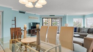 A modern living room with a glass dining table, wicker chairs, a sofa, and a chandelier. - Gulf View, Updated Condo, Steps from the ocean, Short Drive to Shopping (Destin)
