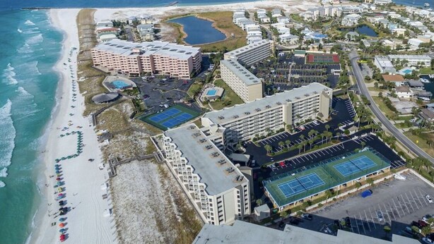 An aerial view of a coastal resort with beachfront hotels, a tennis court, and a marina. - Gulf View, Updated Condo, Steps from the ocean, Short Drive to Shopping (Destin)