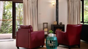 Una habitación con dos sillones de cuero rojo, un taburete color turquesa, una chimenea y vistas a la vegetación a través de amplios ventanales.