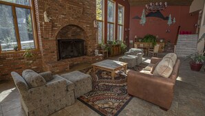 A cozy living room with a brick fireplace, comfortable seating, and large windows offering a view of the outdoors.
