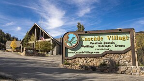 A sign for Cascade Village with a stone wall and a wooden structure in the background.