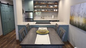 A modern kitchen with teal cabinetry, a stainless steel refrigerator, and a wooden dining table with chairs.