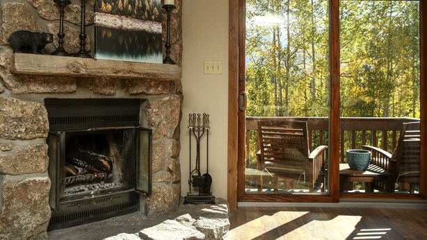 A stone fireplace with a painting above it, a wooden bench, and a view of trees through a glass door.