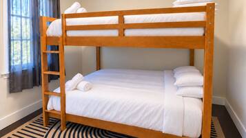 A bunk bed with white bedding, a wooden ladder, and a striped rug.