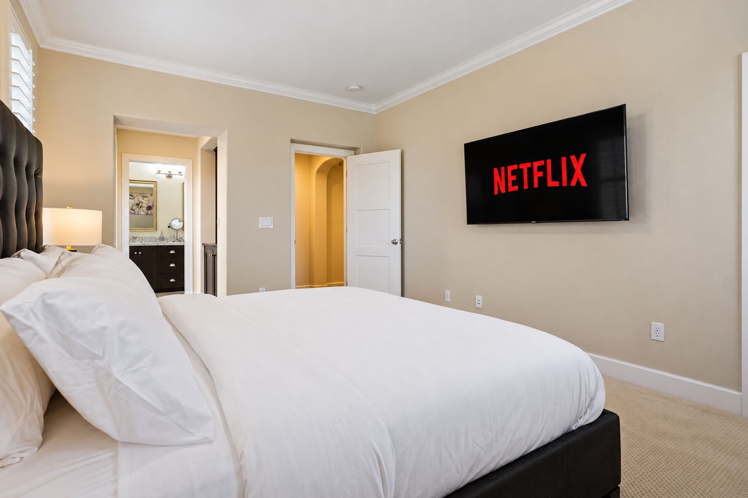 Une chambre d’hôtel avec un grand lit, un téléviseur fixé au mur et une porte donnant sur une autre pièce.