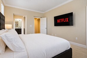 A hotel room with a large bed, a television mounted on the wall, and a door leading to another room. - Spacious 3 Story Home • 4BR • Garage • Balcony • Sleeps 8 (Fremont)