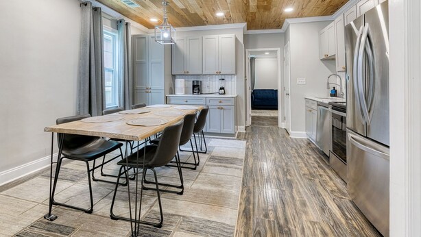 Een moderne keuken met witte kastjes, een houten plafond en een eethoek met een tafel en stoelen.