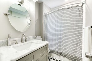 Een badkamer met een witte wastafel, twee kraanwerk, een spiegel en een douchegordijn met strepen.