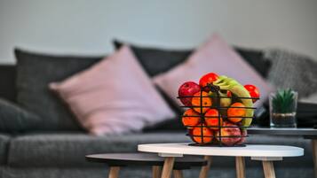 Ein Obstkorb auf einem kleinen Tisch vor einer Couch mit Kissen.