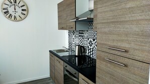 A modern kitchen with wooden cabinets, a black countertop, and a vintage clock on the wall. - LA LOVE LIFE (Mulhouse)