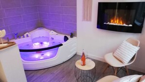 A modern living room with a large, curved jacuzzi tub, a fireplace, and a cozy seating area with a small round table. - LA LOVE LIFE (Mulhouse)