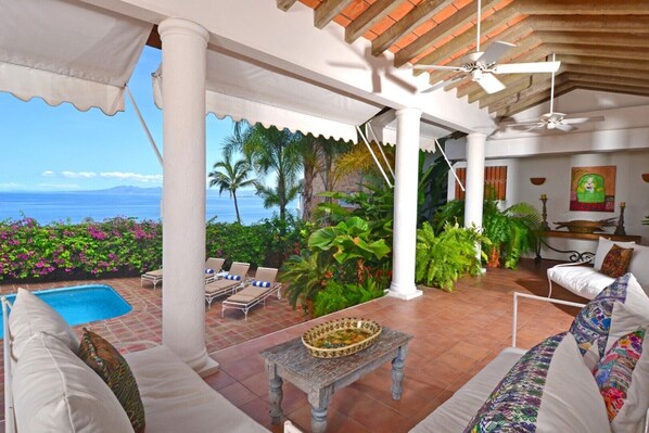 A covered outdoor area with a pool, lounge chairs, and a dining table.