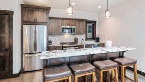 A modern kitchen with dark wood cabinets, stainless steel appliances, a marble island with bar stools, and pendant lighting.