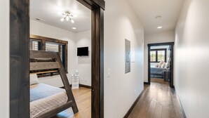 A hallway with a bunk bed, a television, and a door leading to a bedroom with a bed and window.