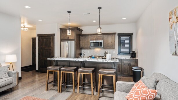 A modern kitchen with a central island, bar stools, wooden cabinets, stainless steel appliances, and pendant lighting.