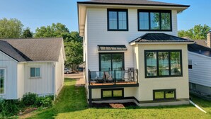 A two-story house with a balcony, a garage, and a well-maintained lawn. - Luxury Lakefront Home w Miles of Lake Views, private pier, lake toys & game room (Pewaukee)