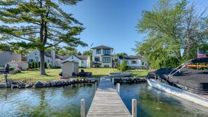 A wooden dock leading to a calm water body with a house and a boat docked on the right. - Luxury Lakefront Home w Miles of Lake Views, private pier, lake toys & game room (Pewaukee)