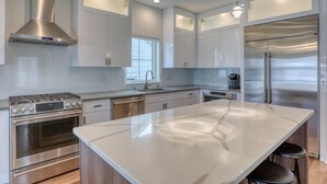 A modern kitchen with stainless steel appliances, white cabinetry, and a large marble island. - Luxury Lakefront Home w Miles of Lake Views, private pier, lake toys & game room (Pewaukee)