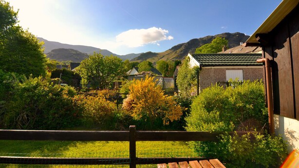 A rural landscape with a wooden fence, a grassy field, and houses with green roofs. - ⭐️Stunning Holiday Home⭐️ - Centre of Coniston - 3 bedroom  (Coniston)