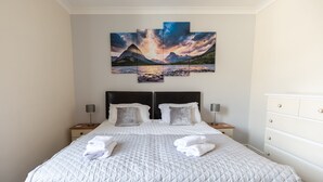 A neatly made bed with a white quilt, two bedside tables with lamps, a white dresser, and a large landscape painting above the bed. - ⭐️Stunning Holiday Home⭐️ - Centre of Coniston - 3 bedroom  (Coniston)