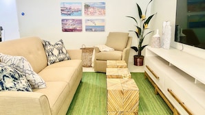 A living room with a beige sofa, a smaller armchair, a coffee table, a TV, and a potted plant. - Sailfish Gulf Suites #4, Garden Views, Steps from the Beach (Holmes Beach)