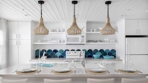 A modern kitchen with white cabinetry, a central island with seating, and decorative blue bowls on the shelves. - Sailfish Gulf Suites #4, Garden Views, Steps from the Beach (Holmes Beach)