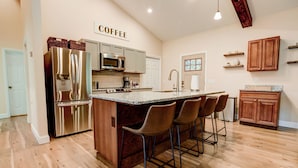 A kitchen with a stainless steel refrigerator, a microwave, a coffee sign, wooden cabinets, and a bar area with stools.