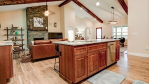 A spacious kitchen with wooden cabinets, a large island, and a stone fireplace.