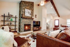 Una sala de estar con chimenea, muebles de cuero, televisor y estantería.