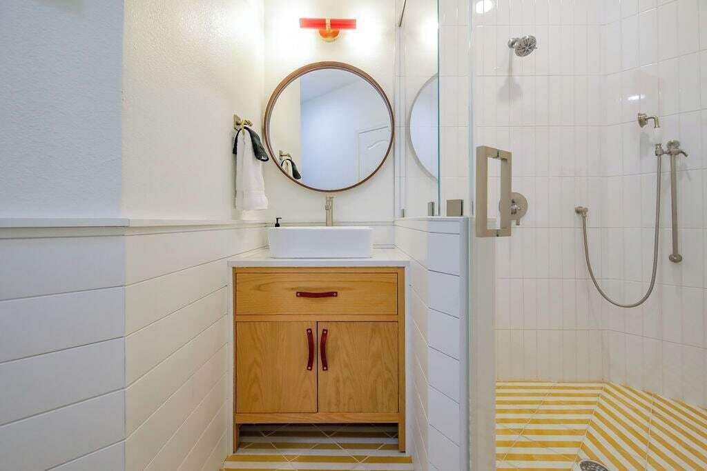 A bathroom with a white sink, wooden cabinet, and a shower area with yellow and white striped tiles.